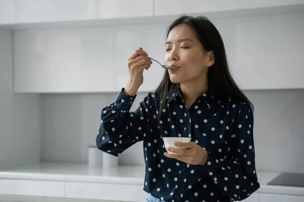 Mujer asiática joven come yogur fresco para el desayuno en la cocina — Foto de Stock