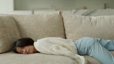 Bitkin düşmüş genç Asyalı kadın kanepeye düşüyor. Yorgun, tembel bir kadın evde tek başına kanepede uyuyor..