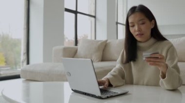 Kredi kartı tutan ve dizüstü bilgisayar kullanan genç bir Asyalı kadın. Evden çalışan bir kadın girişimci var. Çevrimiçi alışveriş, evde çalışma kavramı