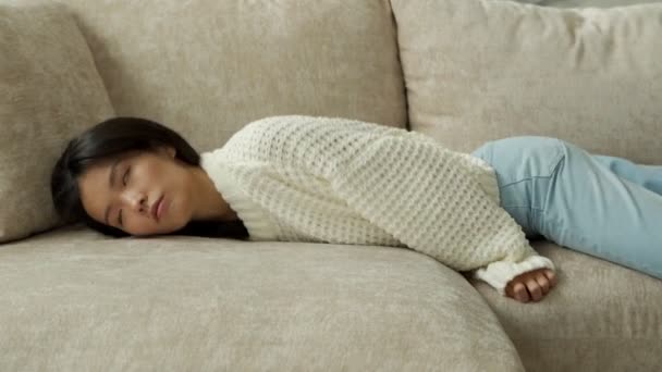 疲れ切った若いアジアの女性がソファの上に落ちます。疲れた怠惰な女性が家だけでソファの上で寝ている. — ストック動画