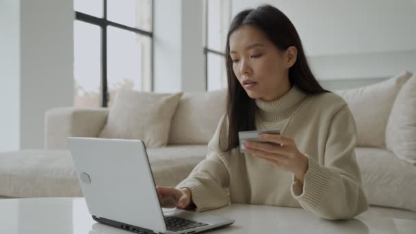 An Asian woman shopping online using a laptop while holding a credit card. The concept of online payments. — Stock Video