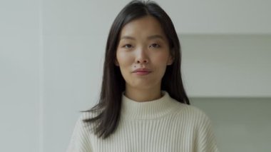 Genç Asyalı kadın, virüs ve enfeksiyon hastalıklarına karşı tıbbi bir maske takıyor ve kameraya bakıyor..