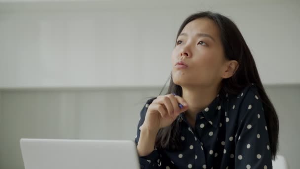 思考の若いビジネスアジアの女性は、ラップトップで作業しながら、ペンを保持し、窓の外を見て — ストック動画