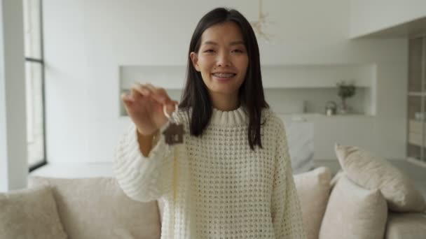 Die junge asiatische Käuferin blickt mit dem Schlüssel in der Hand in die Kamera. Eine glückliche Frau, die stolz darauf ist, eine Wohnung zu kaufen — Stockvideo