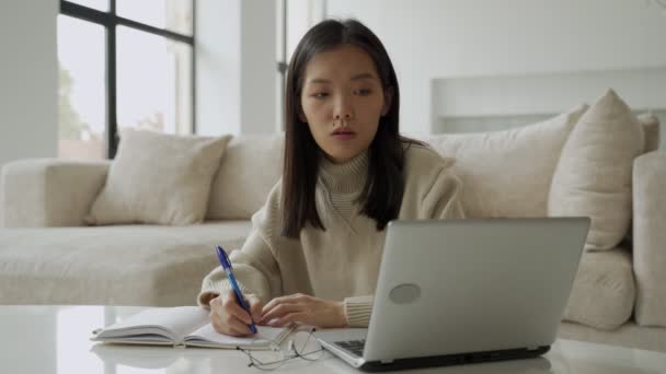 Una joven estudiante asiática está usando una computadora y una tableta. Una joven mujer de negocios está sentada en un escritorio y tomando notas en un cuaderno. Concepto de educación y tecnología. — Vídeo de stock