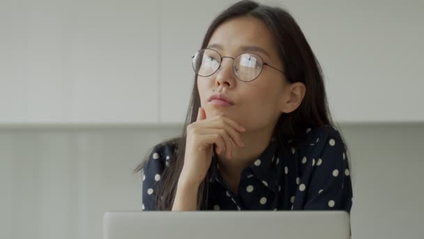 ラップトップで作業している眼鏡を持つ思慮深いアジアの実業家は、距離を見ています。学生は仮想eラーニングリソースを使用します — ストック動画