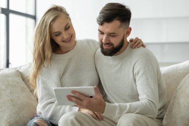 Genç mutlu çift tablet ekrana bakıyor, rahat bir kanepede dinleniyorlar. Birbirine aşık bir çift internetten online alışveriş yapıyor..