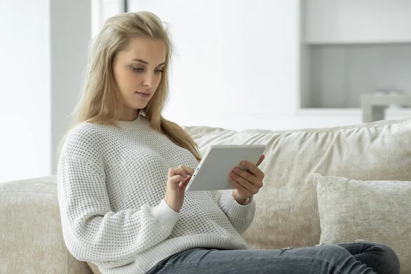 Mujer embarazada feliz utiliza una tableta digital mientras está sentado en el sofá en la sala de estar — Foto de Stock