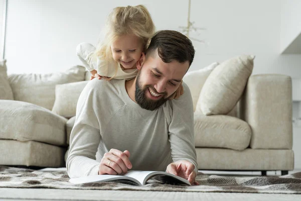 Baard vader leest een sprookje voor zijn dochtertje liggend op de vloer van het huis. Gelukkig gezin liggend op de woonkamer verdieping — Stockfoto