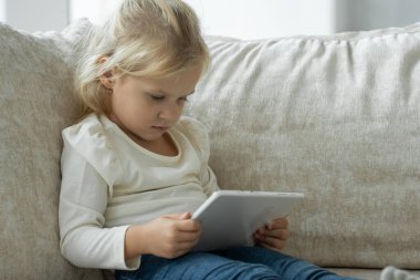 Kanepede oturup çizgi film izlerken ya da internette gezinirken dijital tablet kullanan küçük bir kız.