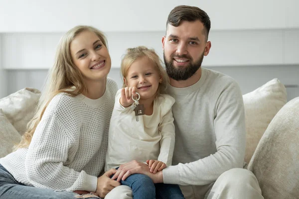 Klein meisje heeft de sleutels van een nieuw ouderlijk huis in haar handen. Portret van een lachend jong getrouwd stel en een schattig meisje met de sleutels — Stockfoto