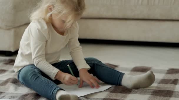 Oplettend meisje van kleuterschool leeftijd, zittend op de vloer in een gezellig appartement, tekent grappige plaatjes met kleurpotloden — Stockvideo