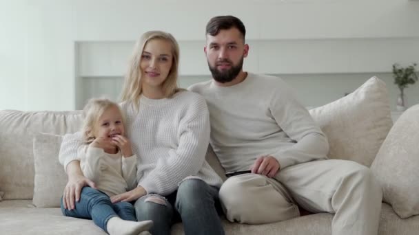 Porträt einer charmanten Familie, Mutter, Vater und kleine Tochter sitzen auf der Couch und sehen einen gruseligen Film — Stockvideo