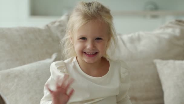 Evde kanepede oturan sevimli bir kızın gülüşü. Küçük bir çocuk gülümser ve kameraya bakar. — Stok video
