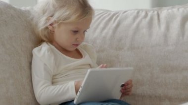 Kanepede oturup çizgi film izlerken ya da internette gezinirken dijital tablet kullanan küçük bir kız.