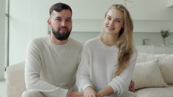 Krásný mladý šťastný pár sedí doma na gauči a dívá se do kamery. Na gauči sedí vousatý muž se svou ženou. — Stock video