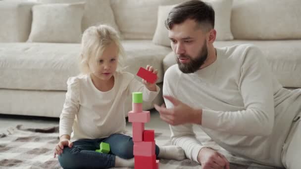 Veselý otec a dcera hrají kostky společně doma, sedí na podlaze v obývacím pokoji. — Stock video