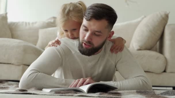 Baard vader leest een sprookje voor zijn dochtertje liggend op de vloer van het huis. Gelukkig gezin liggend op de woonkamer verdieping — Stockvideo