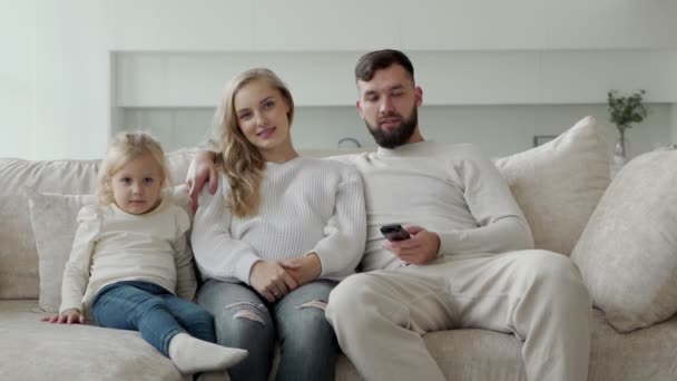 Jovens pais e sua filhinha bonitinha estão assistindo a um interessante documentário informativo em casa no sofá — Vídeo de Stock