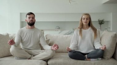 Sakin genç aile birlikte yoga yapıyor, kanepede lotus pozisyonunda oturuyor. Ebeveynler kanepede dinlenir, meditasyon yaparlar.