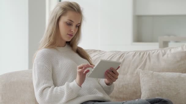幸せな妊娠中の女性はリビングルームでソファに座っている間、デジタルタブレットを使用します — ストック動画