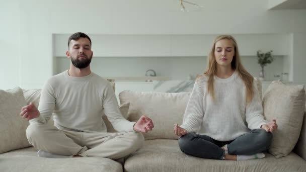 Sakin genç aile birlikte yoga yapıyor, kanepede lotus pozisyonunda oturuyor. Ebeveynler kanepede dinlenir, meditasyon yaparlar. — Stok video