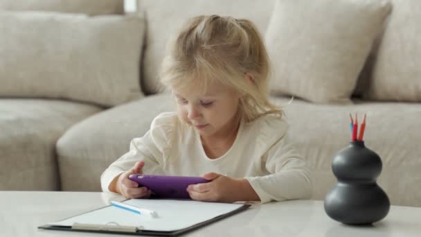 Χαριτωμένο κοριτσάκι με ένα smartphone στον καναπέ στο δωμάτιο παίζοντας παιχνίδια — Αρχείο Βίντεο