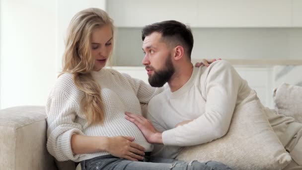 Lächelnder Mann streicht seiner schwangeren Frau über den Bauch. Schwangere und Ehemann halten sich an den Händen. Das Konzept der Gesundheitsfürsorge und die Liebe zur Schwangerschaft. — Stockvideo