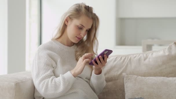 興奮した妊婦が携帯電話を見ている。電子メールで良いニュースを受信し、リビングルームでソファに座っている間に成功を祝う興奮妊婦 — ストック動画