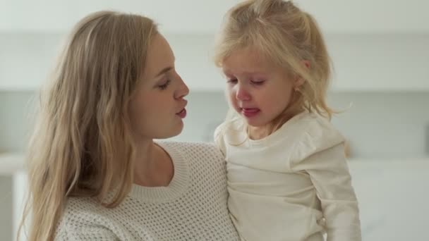 Kind weint im Zimmer in den Armen seiner Mutter. Die junge Mutter versucht ihre weinende kleine Tochter zu beruhigen. Das Konzept der Kindererziehung. — Stockvideo
