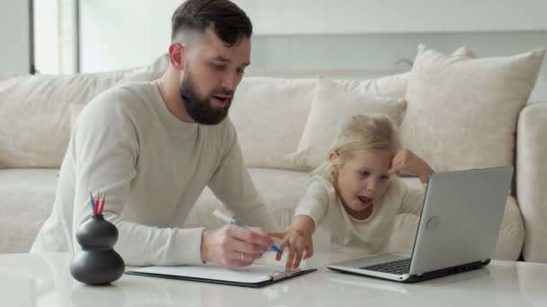Giovane padre insegna a una giovane figlia utilizzando un computer portatile vicino al divano nel soggiorno della casa — Video Stock