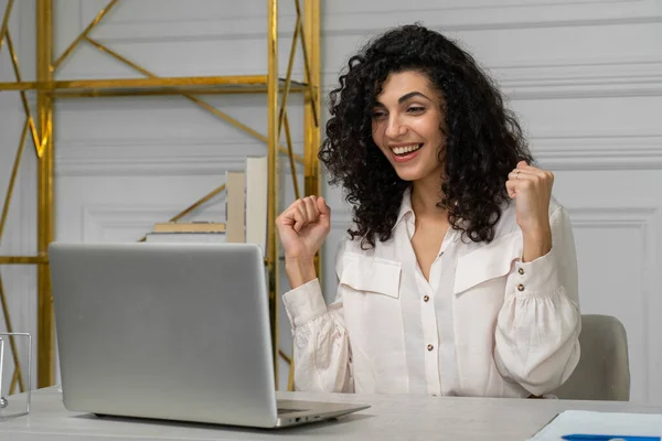 Un empleado indio emocionado mira la pantalla de la computadora portátil, lee las buenas noticias. Una joven y feliz mujer étnica recibe triunfalmente un agradable mensaje en la computadora — Foto de Stock