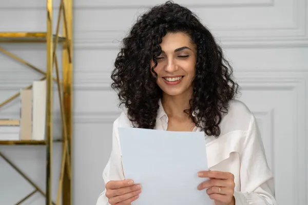 Счастливая этническая женщина с кудрявыми черными волосами читает письмо с хорошими новостями, отличным предложением, возможностью получить работу — стоковое фото