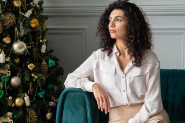 Mutlu, rüya gibi, kıvırcık saçlı, siyah saçlı kadın Noel ağacının yanında oturuyor, uzaktan bakıyor, bir dilek tutuyor. Gülümseyen genç bir kadın Noel 'in tadını çıkarıyor.
