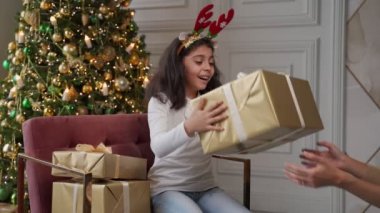 Anne eli, küçük kızına Noel hediyesi veriyor. Kızın elinde bir hediye kutusu var ve hediyeyle mutlu..