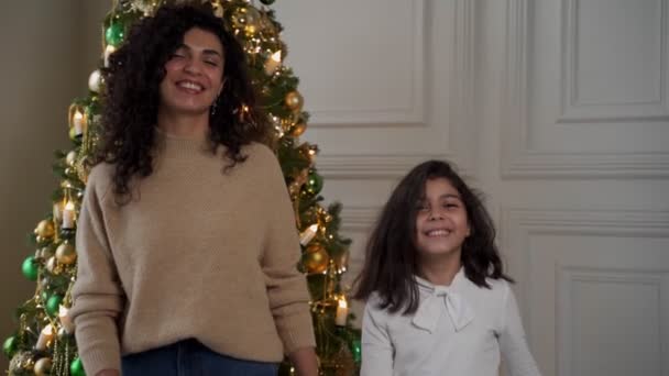 Mujer y su hija miran a la cámara y caminan sobre el fondo de un árbol de Navidad — Vídeo de stock