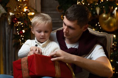 Sevinçten havalara uçmuş baba küçük oğluna sarılıyor, aile Noel 'i kutluyor, hediyeleri açıyor, Noel ağacının yanındaki sandalyeye oturuyor.