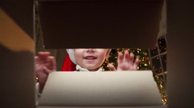 Noel Baba şapkalı mutlu çocuk kutuya bakar, gülümser ve ellerini uzatır. Bir çocuk Noel hediyesi kutusunu açar. Kutudan görüntüle