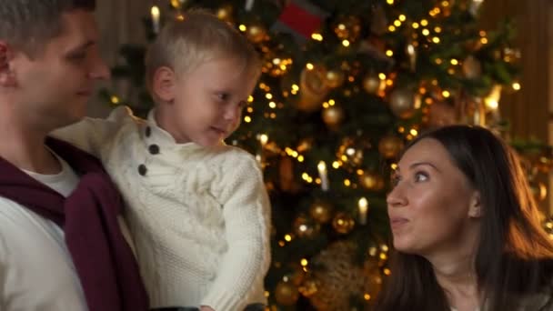 Fiatal család ünnepli a karácsonyt otthon. Egy boldog fiatal család élvezi a nyaralást együtt a karácsonyfa — Stock videók
