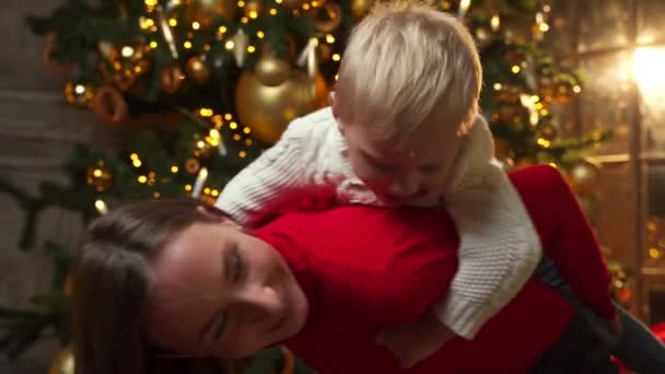 Veselý maminka v červené bundě piggybacking syn zatímco těší vánoční dovolenou doma — Stock video