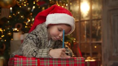 Noel çocuğu Noel Baba 'ya bir mektup yazar. Noel şapkalı bir çocuk bir Noel ağacının arkasına dilek listesi yazar.