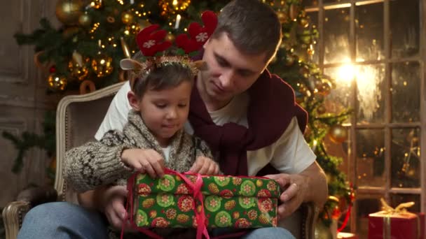 Mignon bébé fils ouvre un cadeau de Noël de son père. Un père offre un cadeau de Noël à son fils. — Video