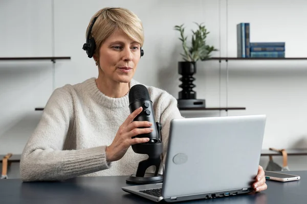 Mujer madura con estilo graba un podcast de audio en su acogedor apartamento en casa — Foto de Stock