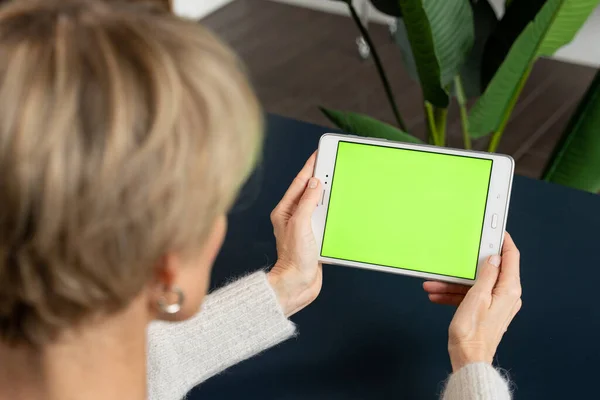 Una mujer de mediana edad está viendo contenido usando una tableta en una pantalla verde — Foto de Stock