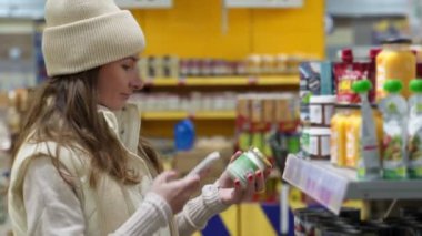 Mağazadaki kadın, barkodu tarayarak akıllı telefondan konserve yiyeceklerin besinlerini kontrol ediyor.