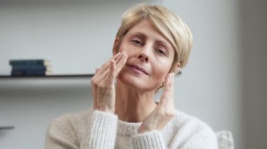 Çekici orta yaşlı bir kadın yanağının tenine dokunuyor, olgun güzellik kavramı.