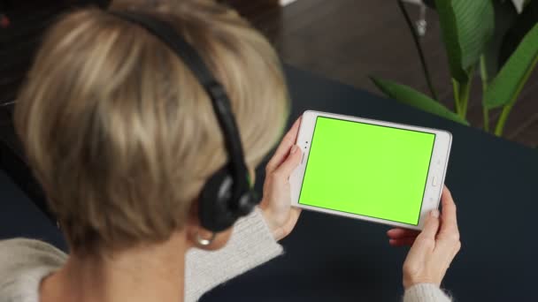 헤드셋을 끼고 있는 한 중년 여성 이 녹색 화면에 태블릿을 사용하여 내용을 보고 있습니다. — 비디오