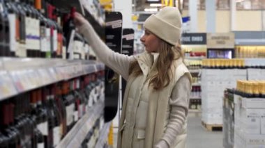 Hangi şarabı alacağına ve süpermarketten alışveriş yapacağına karar veren bir kadın.