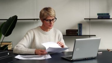 Ofiste dizüstü bilgisayarda çalışan olgun bir iş kadınının portresi, gözlüğünü çıkarıyor ve dizüstü bilgisayarına bakarken düşünüyor.