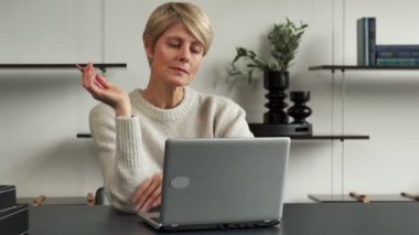 Odaklanmış orta yaşlı bir girişimci kadın modern bir ofis binasında masa başında çalışırken derin düşüncelere daldı.